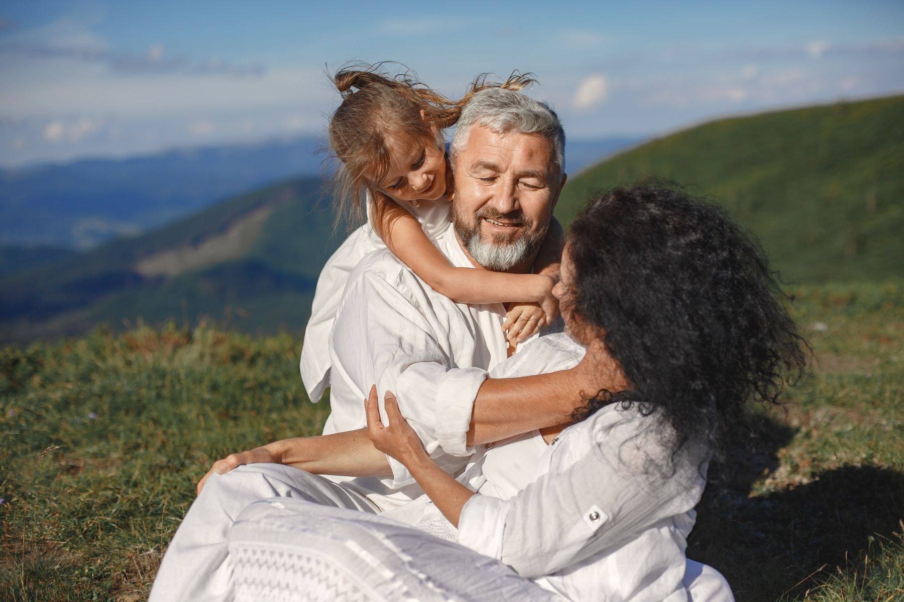 Grandparents embracing their granddaughter in a sunny mountain landscape