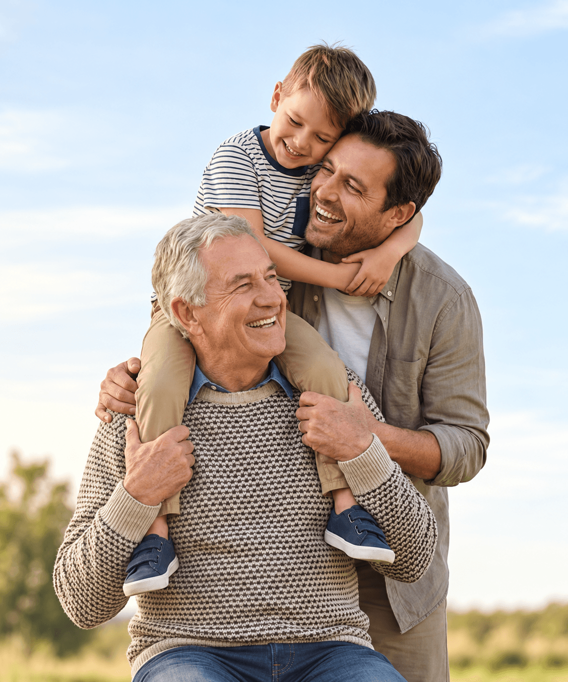 A grandfather, father, and son laughing together outdoors